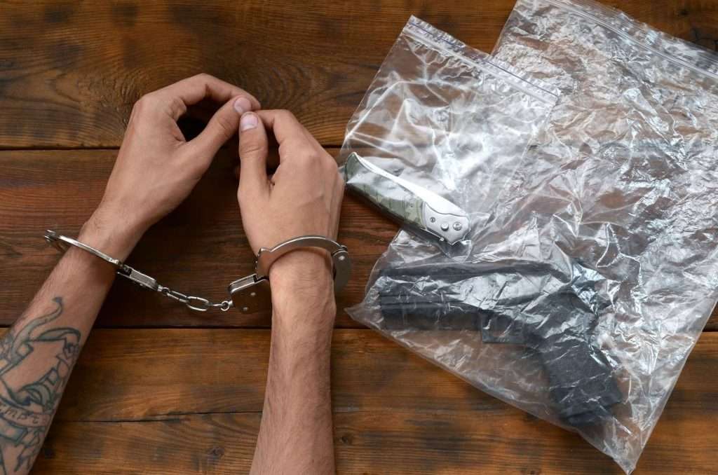 Handcuffed hands of criminal suspect on wooden table and crime scene evidence in transparent plastic
