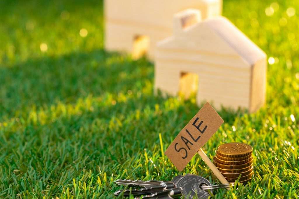 Wooden toy house on grass with sale sign