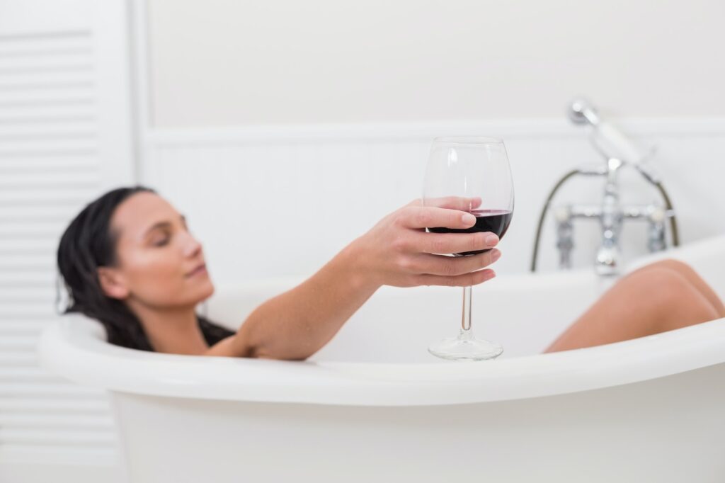 Pretty brunette taking a bath with glass of wine in a bathroom